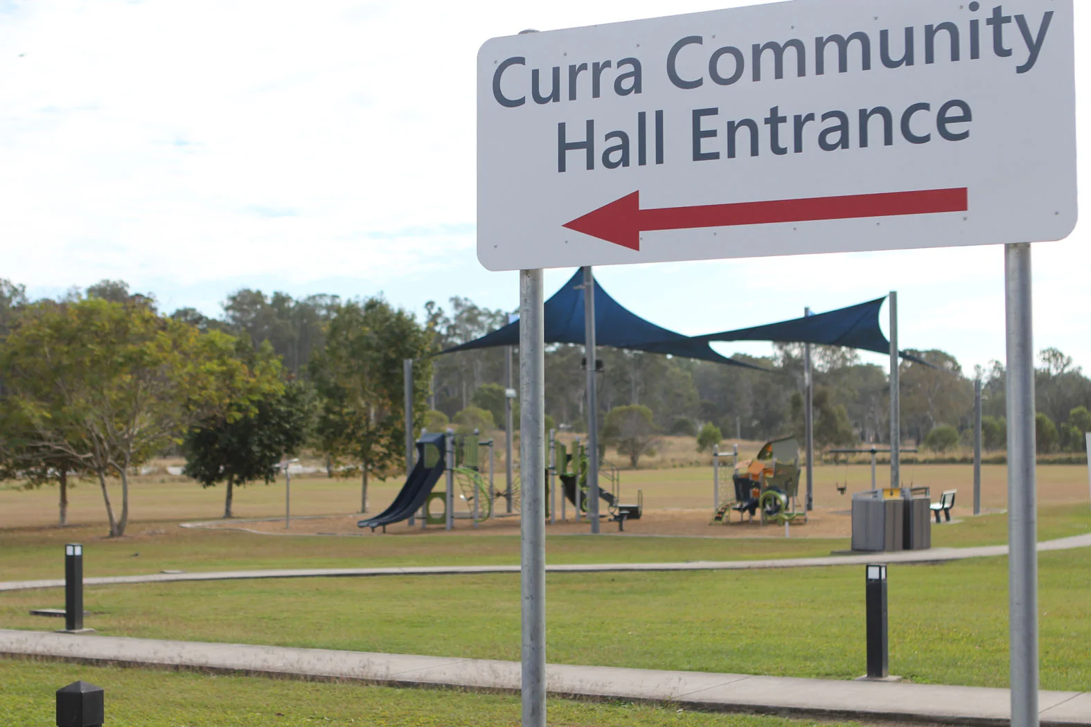 Curra Community Hall entrance sign with the playground and open grounds behind it